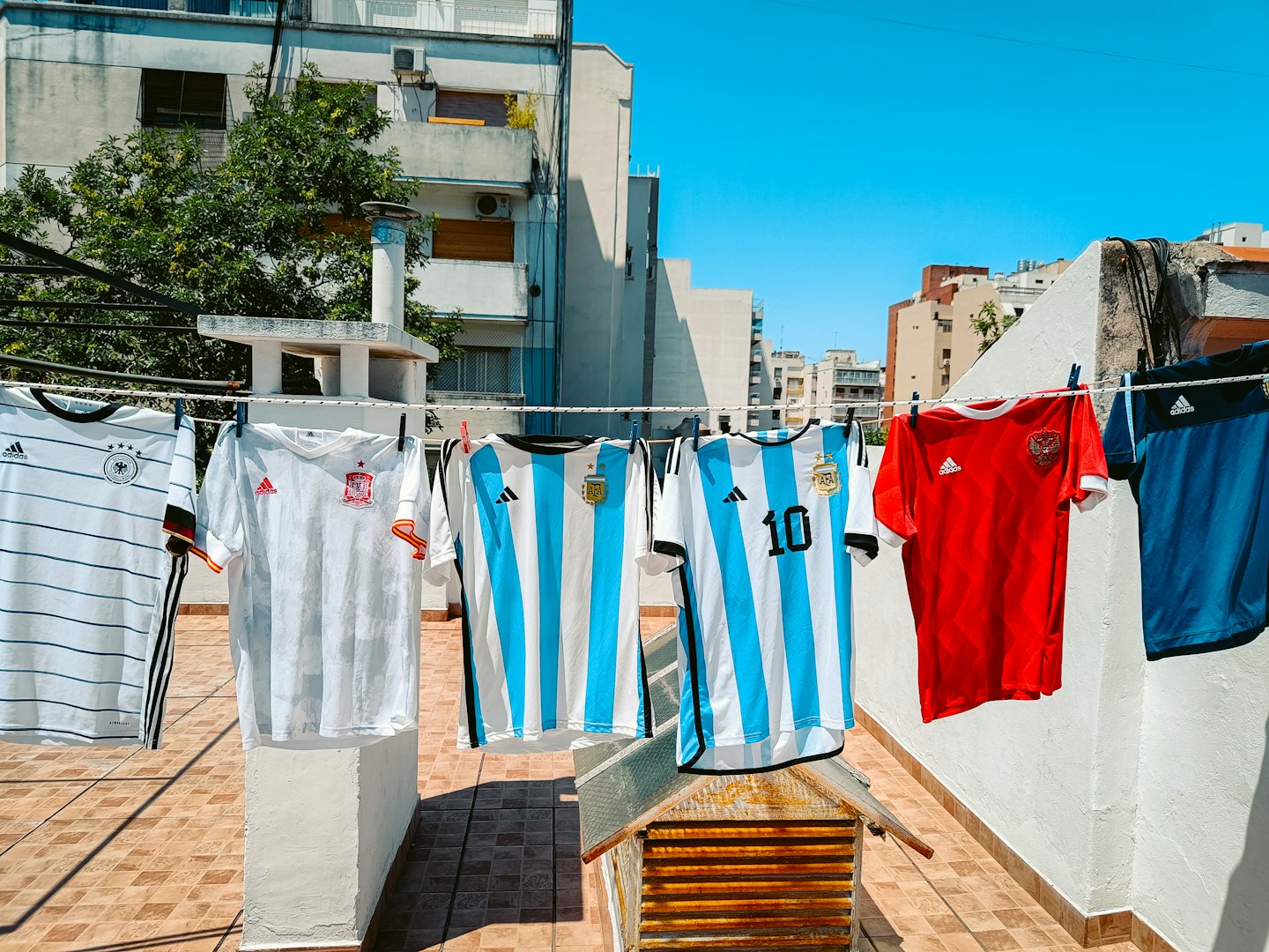 Colorful soccer jerseys hang on a clothesline on a sunny rooftop.